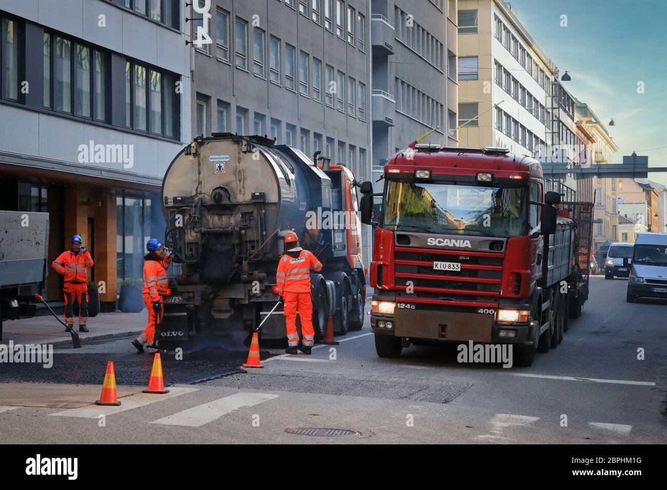 Lavori di strada equipaggio riparazione vecchio asfalto pavimentazione in città. Traffico con Scania 124G trasporto di macchine in transito. Helsinki, Finlandia. 13 maggio 2020. Foto Stock