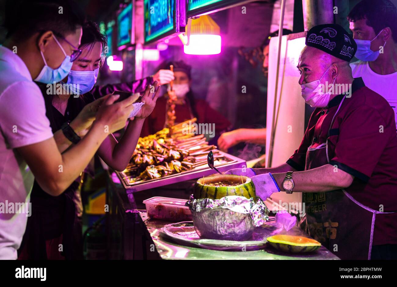 Hotan, la regione autonoma cinese di Xinjiang Uygur. 18 maggio 2020. Un fornitore serve prelibatezze locali ai clienti in una fiera notturna a Hotan, regione autonoma Xinjiang Uygur, nella Cina nord-occidentale, 18 maggio 2020. Con il caldo, le attività turistiche locali si sono gradualmente riprese. Credit: Wang Fei/Xinhua/Alamy Live News Foto Stock