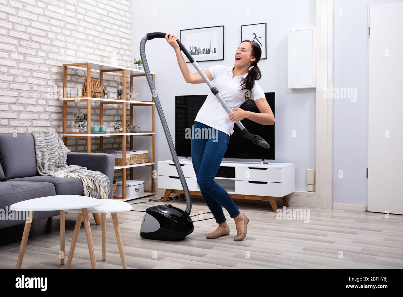 Felice bidello femmina ballando con aspirapolvere a casa Foto Stock