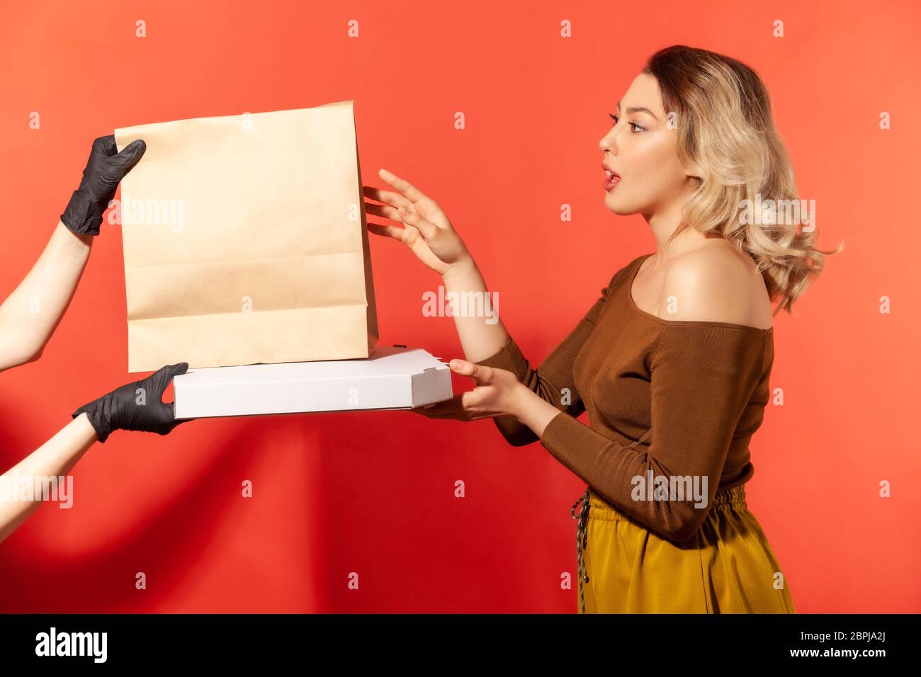 Donna che prende sacchetto della spesa e pizza da mani del corriere in guanti protettivi, consegna sicura del cibo in quarantena, prevenzione del coronavirus 2019-ncov. Rimanere h Foto Stock