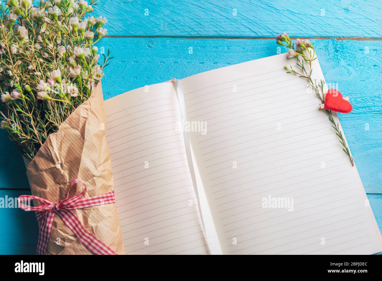 Aprire le pagine del notebook con minuscoli fiori bianchi bouquet e a forma di cuore clip in legno, su uno sfondo blu. Wedding planning contesto. Donne giorno telaio. Foto Stock