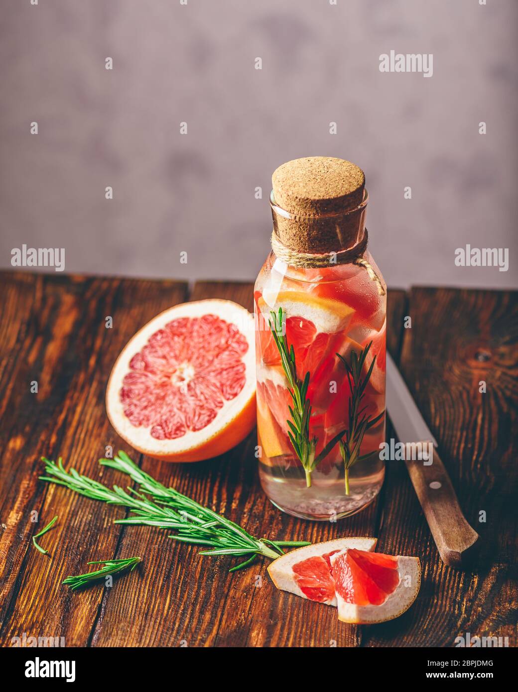 Bottiglia di acqua infusa con fette di materie di pompelmo e di molle di fresco di rosmarino. Orientamento verticale. Foto Stock