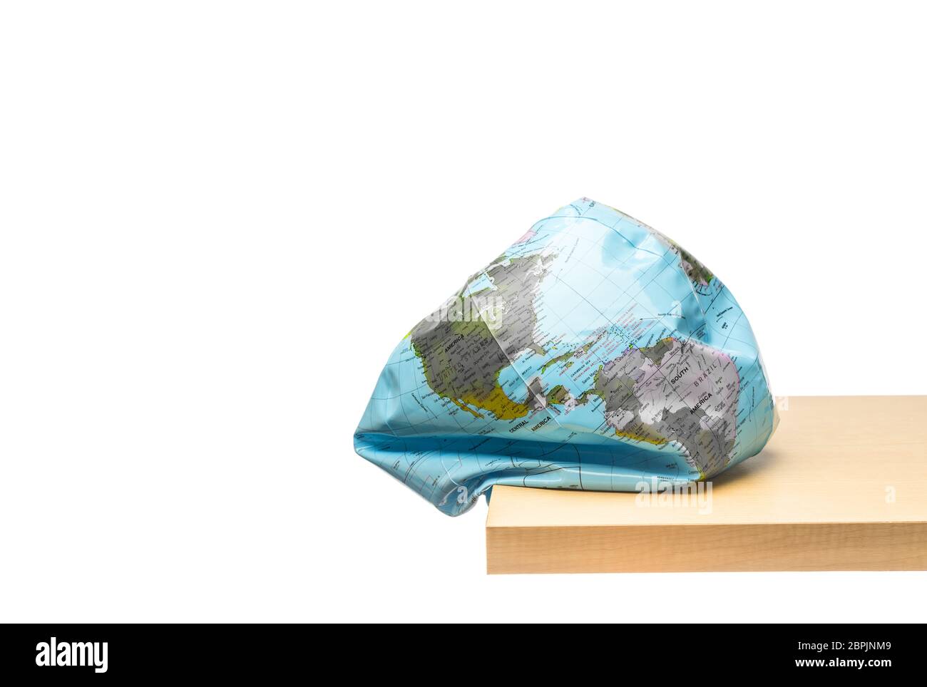 Appiattimento della terra globo al bordo del tavolo di legno su sfondo bianco, concetto di danno ambientale Foto Stock