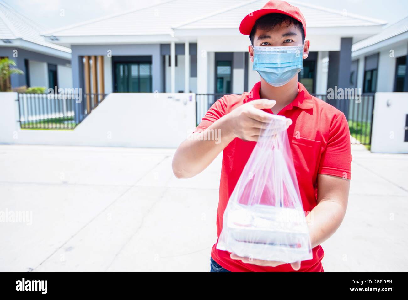 I militari asiatici che indossano una divisa rossa con un cappuccio rosso e una maschera facciale che manipolano le scatole degli alimenti in sacchetti di plastica da dare al cliente davanti a t Foto Stock