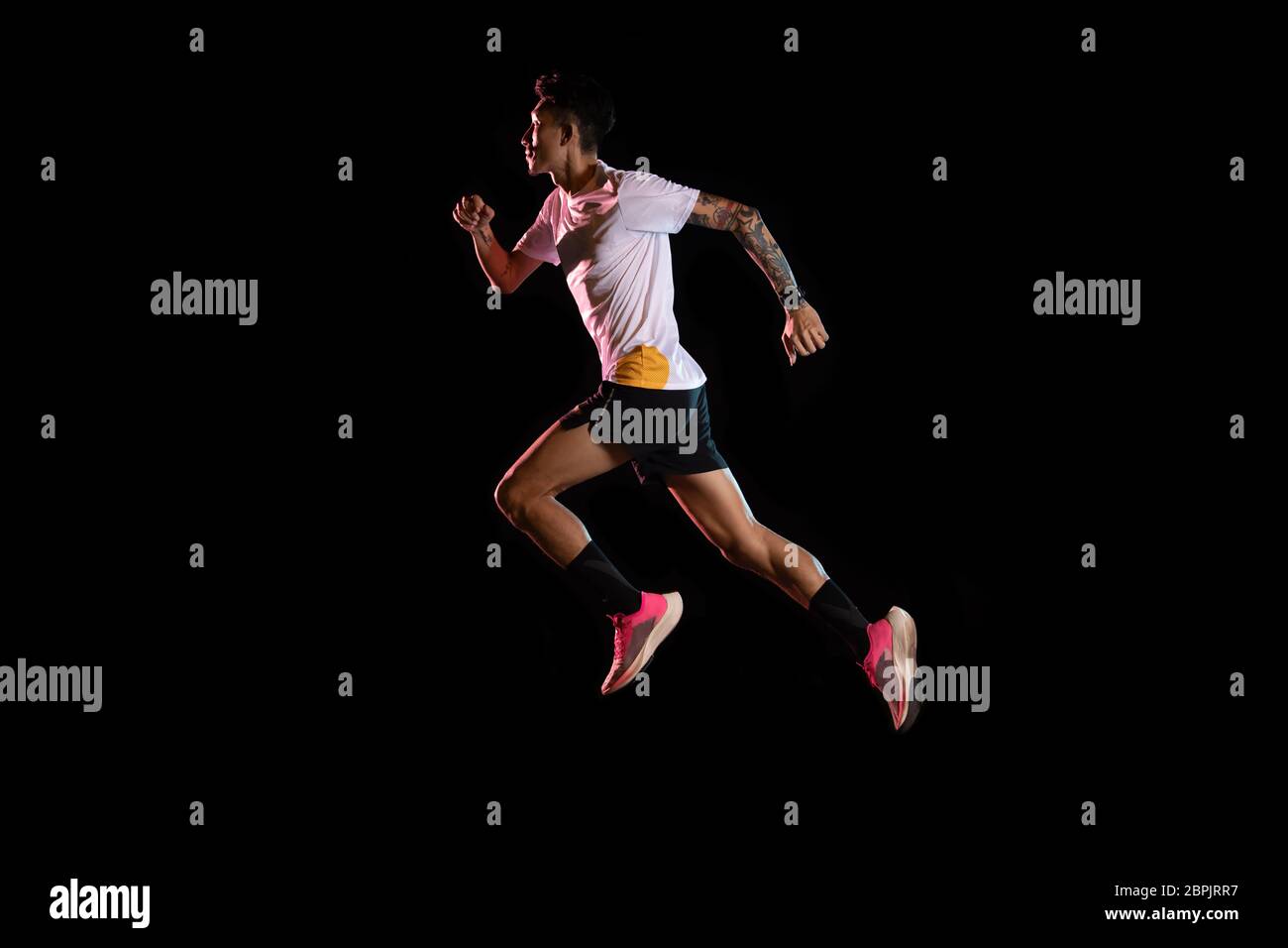Giovane corridore sprinter asiatico uomo che corre in studio su sfondo nero Foto Stock