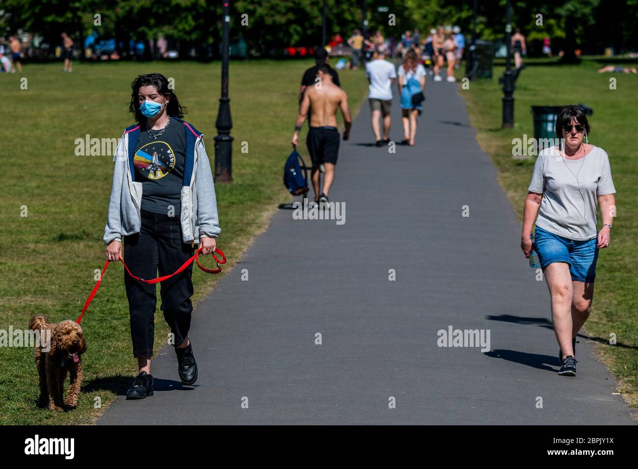 Londra, Regno Unito. 19 maggio 2020. Una delle uniche persone in una maschera - le persone godono il sole su Clapham comune dopo che il governo ha allentato le restrizioni e permesso alle persone di incontrarsi - Lambeth Consiglio hanno sostituito i segni per dire stare attenti e per consentire alle persone di sedersi sulle panchine. Il "blocco" continua per l'epidemia di Coronavirus (Covid 19) a Londra. Credit: Guy Bell/Alamy Live News Foto Stock