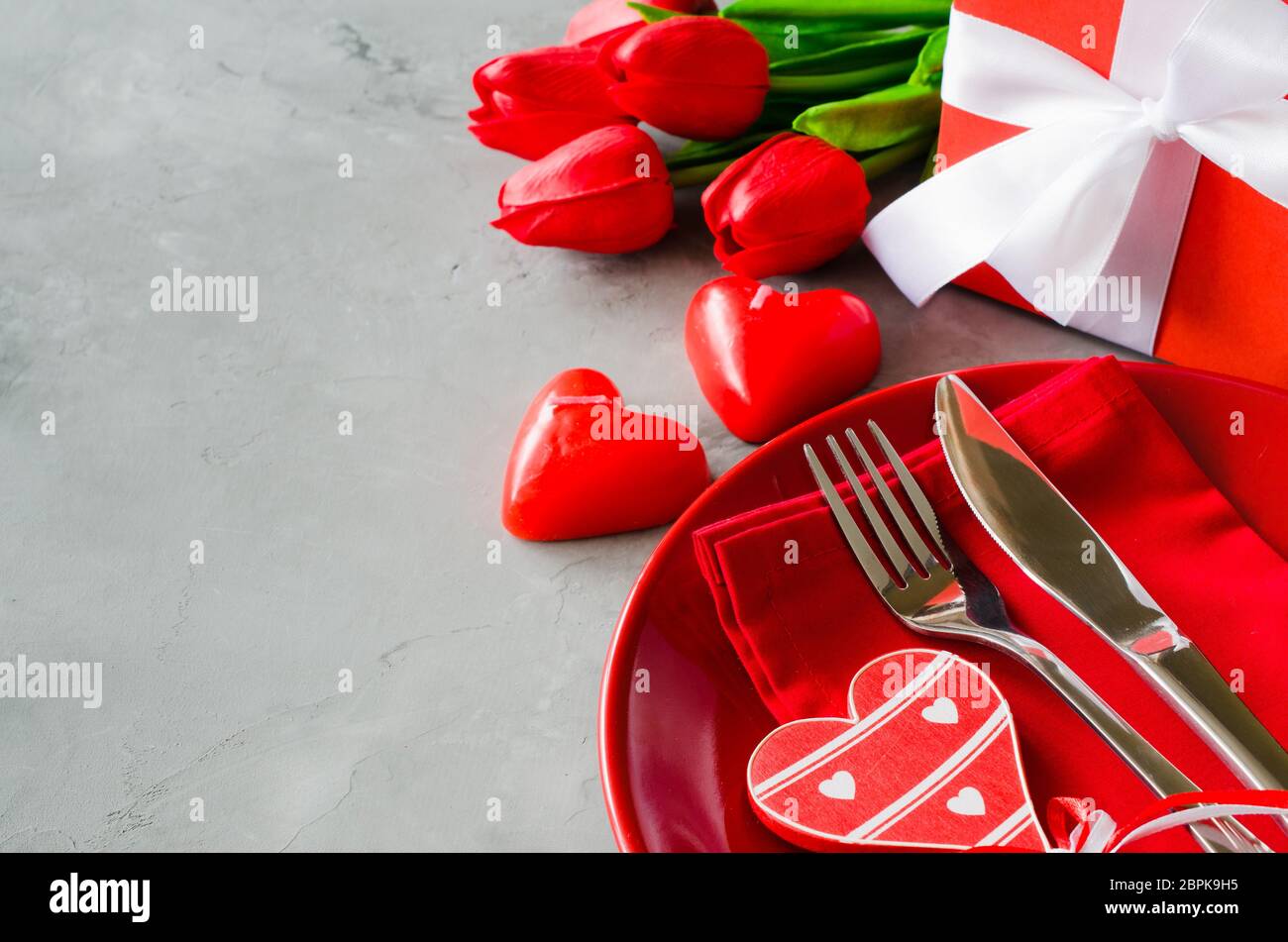 Tavola festiva impostazione per il giorno di San Valentino con scatola regalo, tulipani e candele in forma di cuori. Foto Stock