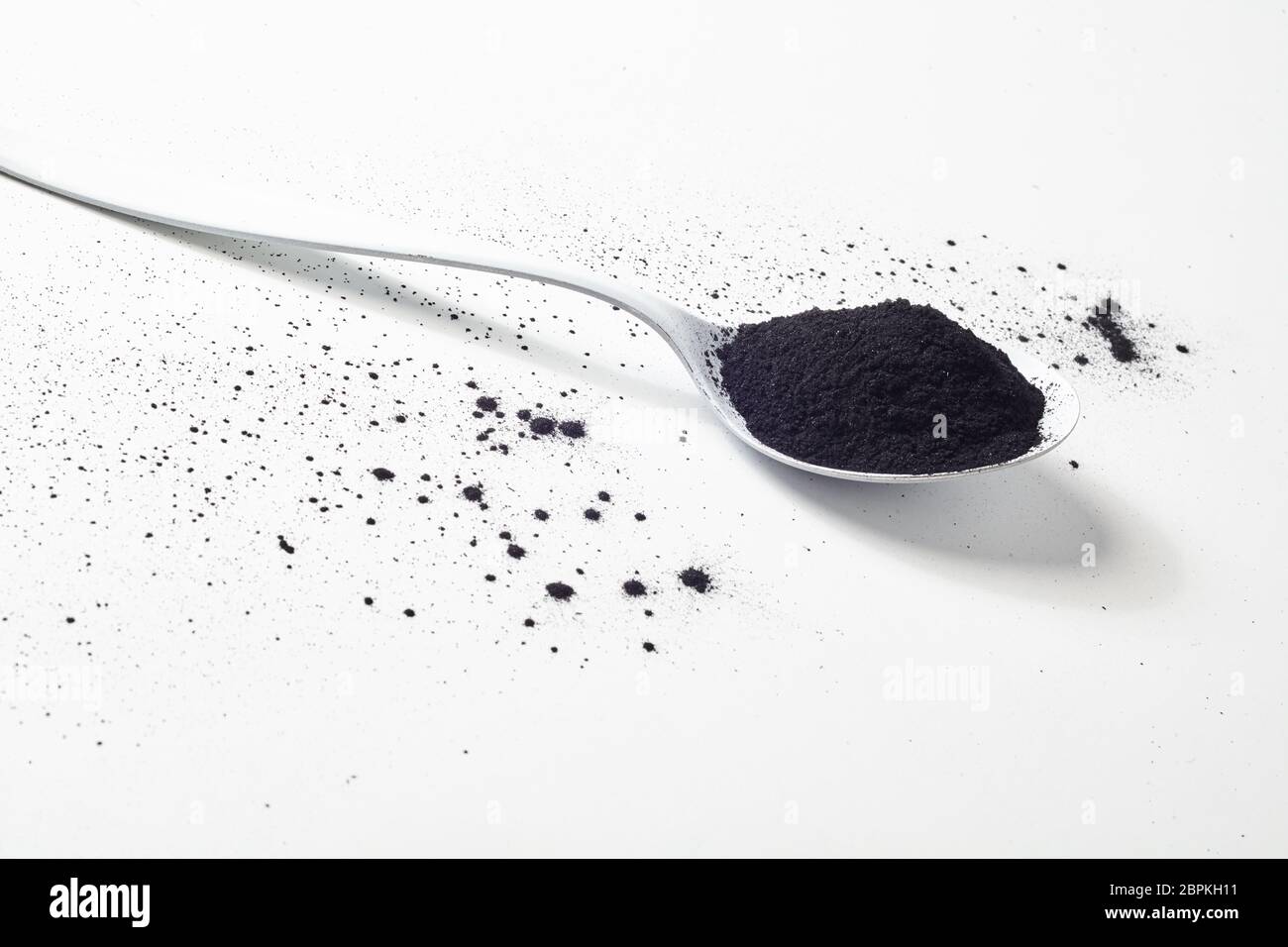 Un cucchiaio di polvere di carbone su sfondo bianco con un po' di polvere  nera sparsi intorno. Vista da un angolo alto Foto stock - Alamy