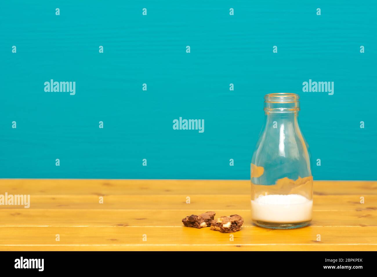 Un terzo pinta bicchiere di latte bottiglia piena a metà con fresco latte cremoso e pezzetti di cioccolato sbriciolati, su di un tavolo di legno contro un sfondo teal Foto Stock