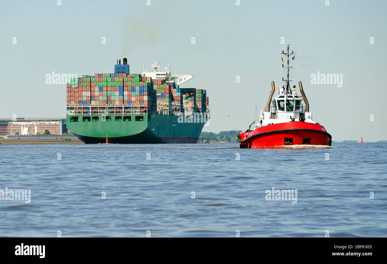 Nave container che parte e barca a rimorchio porto di ritorno al ormeggio sul fiume Elba ad Amburgo, Germania Foto Stock