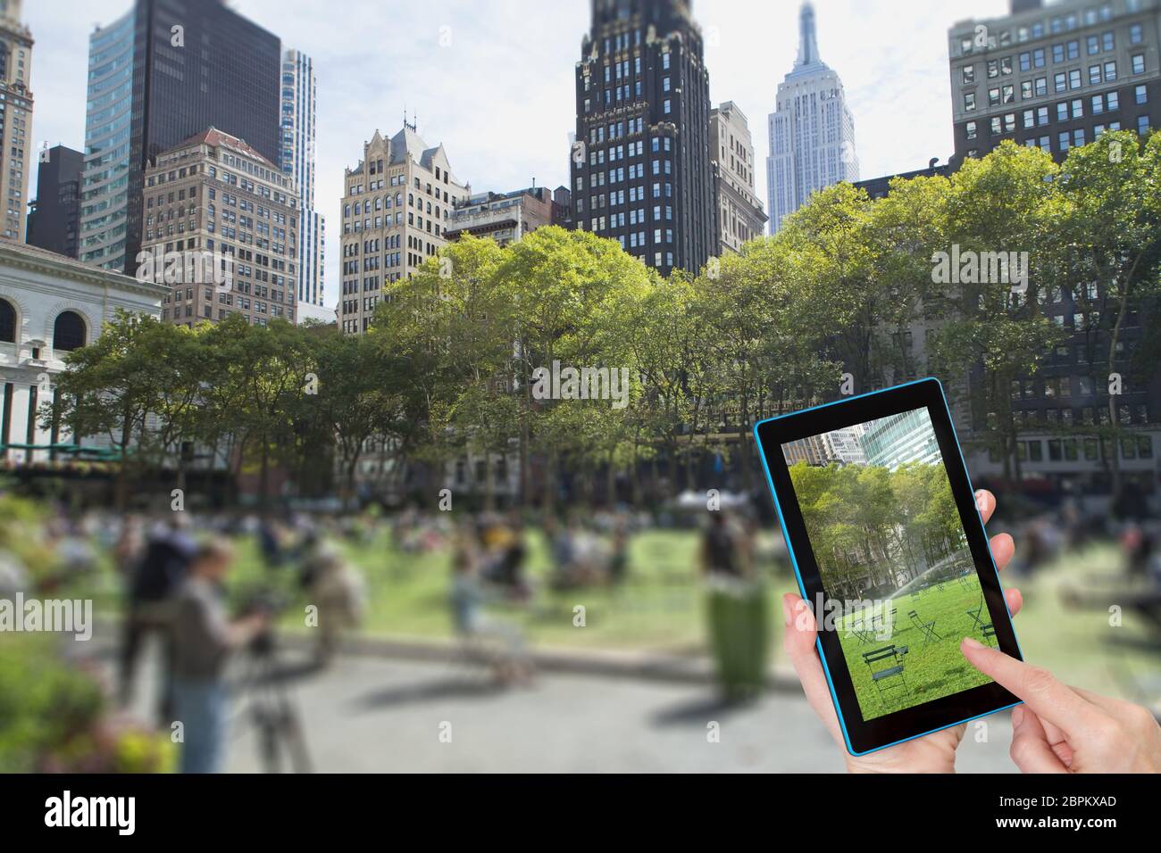 Dito femmina toccando tablet con vuoto Bryant Park immagine sullo schermo. Intenzionalmente immagine sfocata di un Bryant Park (NYC) è in background. Un Foto Stock