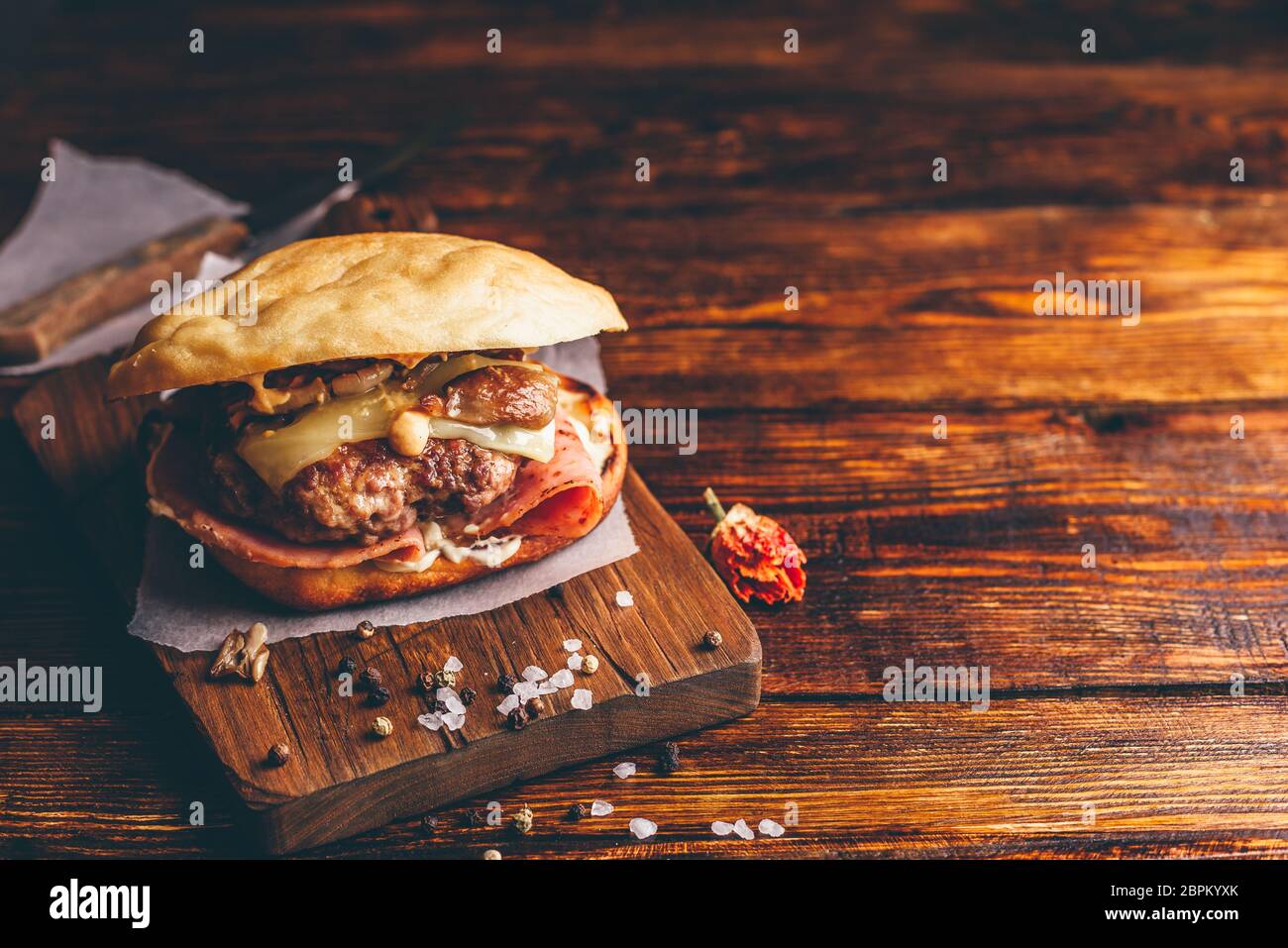 In casa Burger sul bordo di taglio. Cheeseburger con carne di manzo Patty, Wisconsin il formaggio svizzero, prosciutto, funghi saltati, Dijon senape, maionese e Potato R Foto Stock