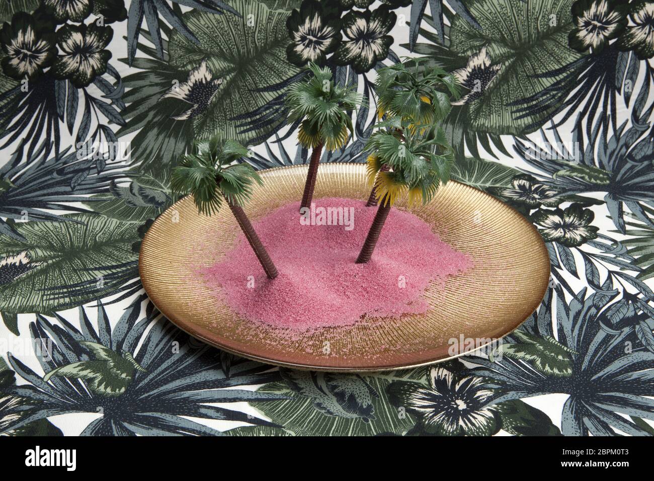 Sabbia rosa e le palme in un piatto dorato su uno sfondo tropicale. Il minimo di still life fotografia a colori., Foto Stock