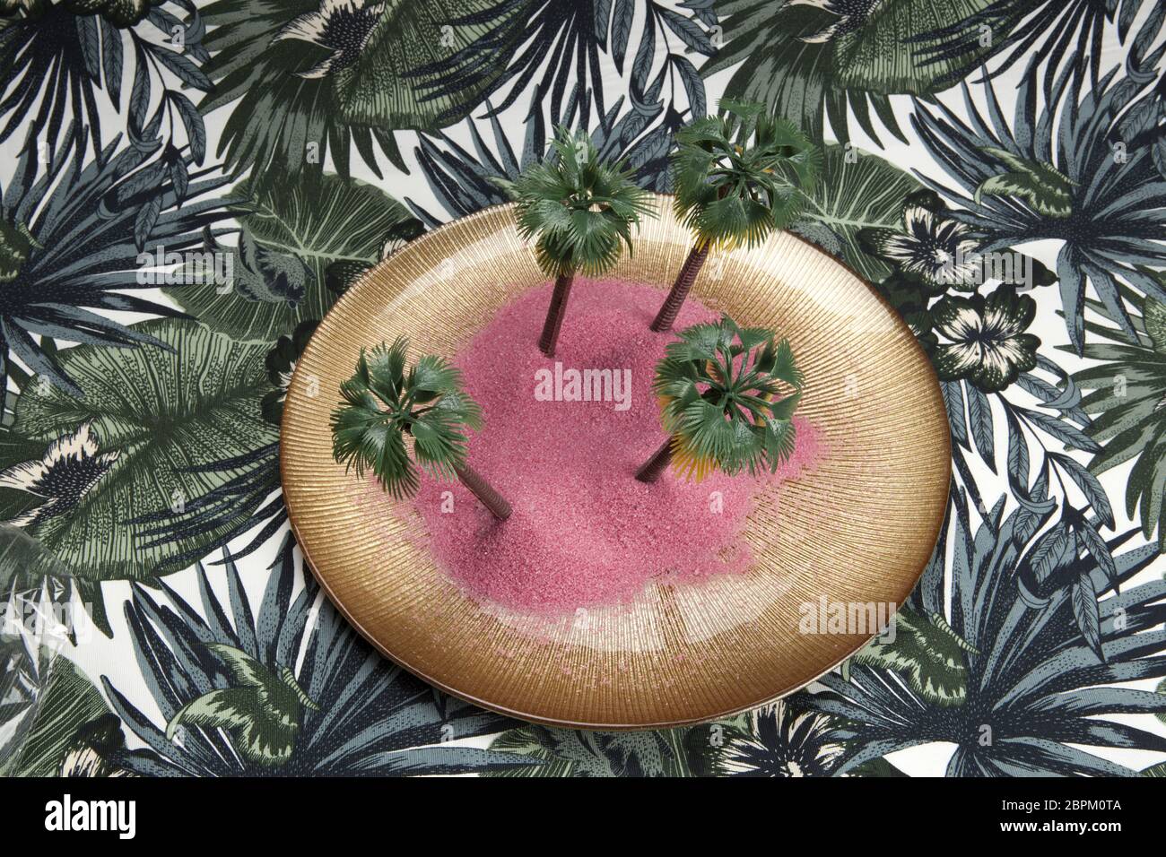 Sabbia rosa e le palme in un piatto dorato su uno sfondo tropicale. Il minimo di still life fotografia a colori., Foto Stock
