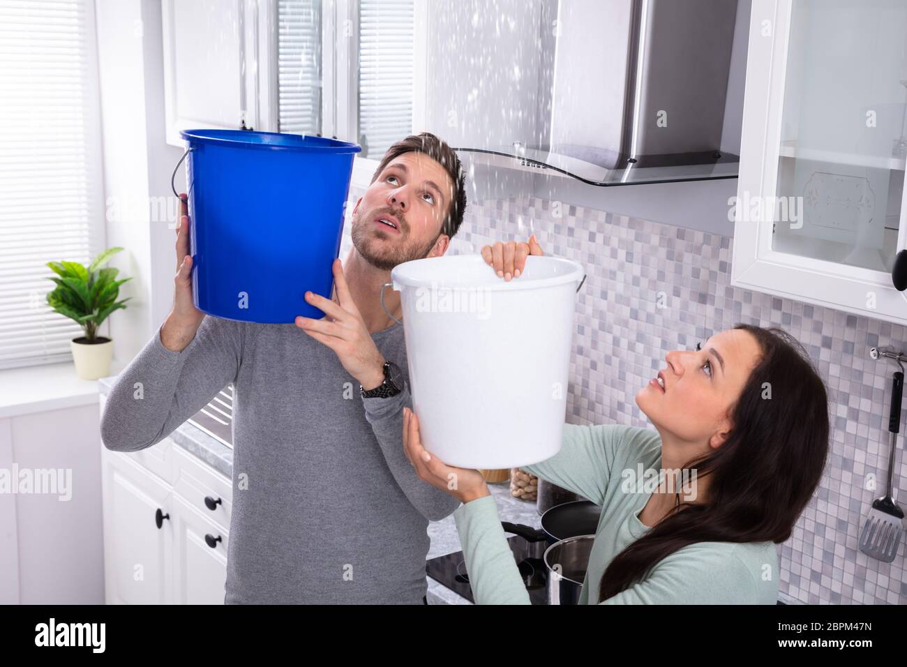 Close-up di un preoccupato coppia giovane la raccolta di perdite di acqua dal soffitto nel secchio blu Foto Stock