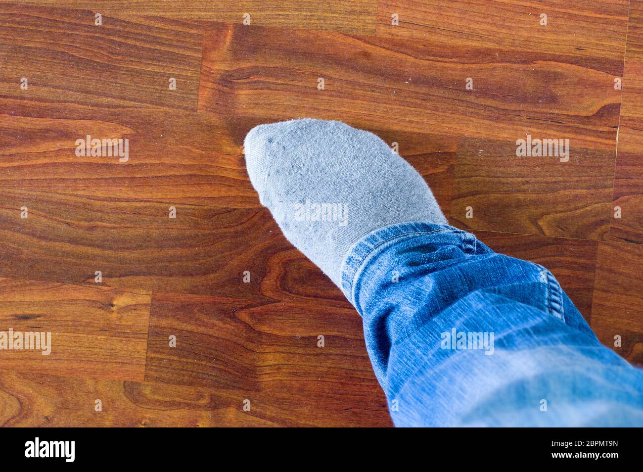 Gambe di un uomo in jeans blu con calze grigie su un pavimento di legno Foto Stock