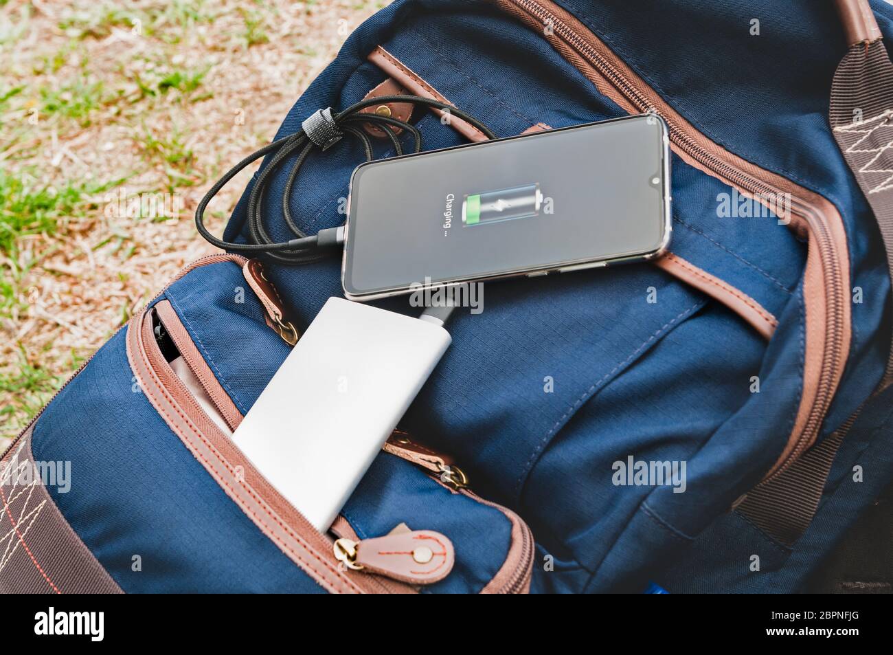 Il moderno smartphone viene caricato da una banca elettrica mentre si sdraia sullo zaino durante un'escursione. Concetto di stile di vita Foto Stock