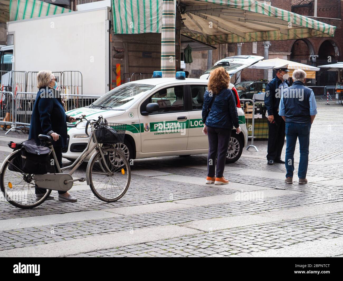 Cremona, Lombardia, Italia - Maggio 2020 persone locali che indossano maschera facciale protettiva in linea e controlli più severi della polizia all'accesso al mercato stradale Foto Stock