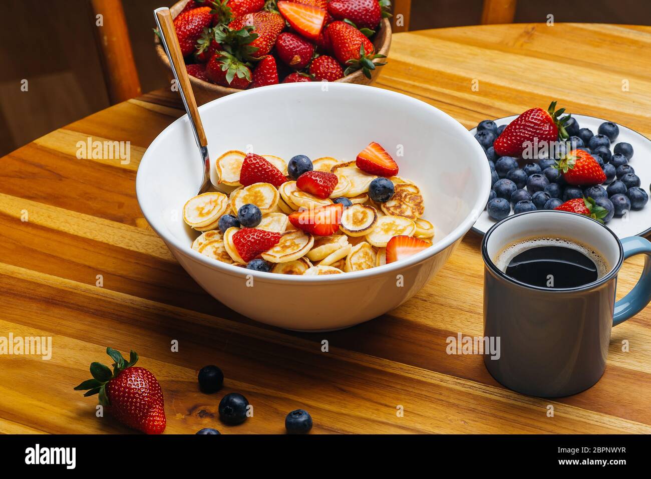 Minuscoli pancake per colazione. Frittelle con fragole e mirtilli cucinati la mattina per la colazione nella cucina casalinga. Cibo sfondo. Foto Stock