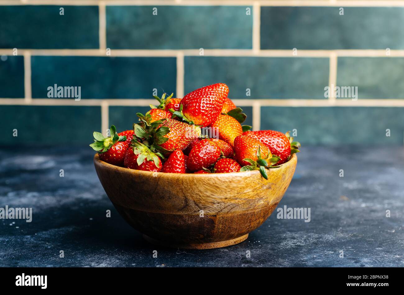 Fragole in un recipiente. Fragole fresche in una ciotola di legno sullo sfondo della cucina. Bacche, frutta, cibo di fondo Foto Stock