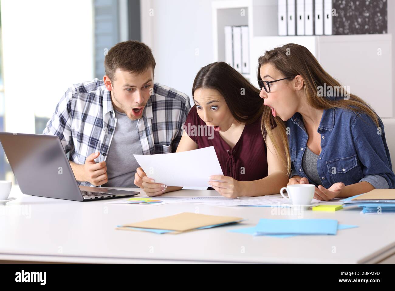 Tre dipendenti stupito la lettura di un documento cartaceo in ufficio Foto Stock