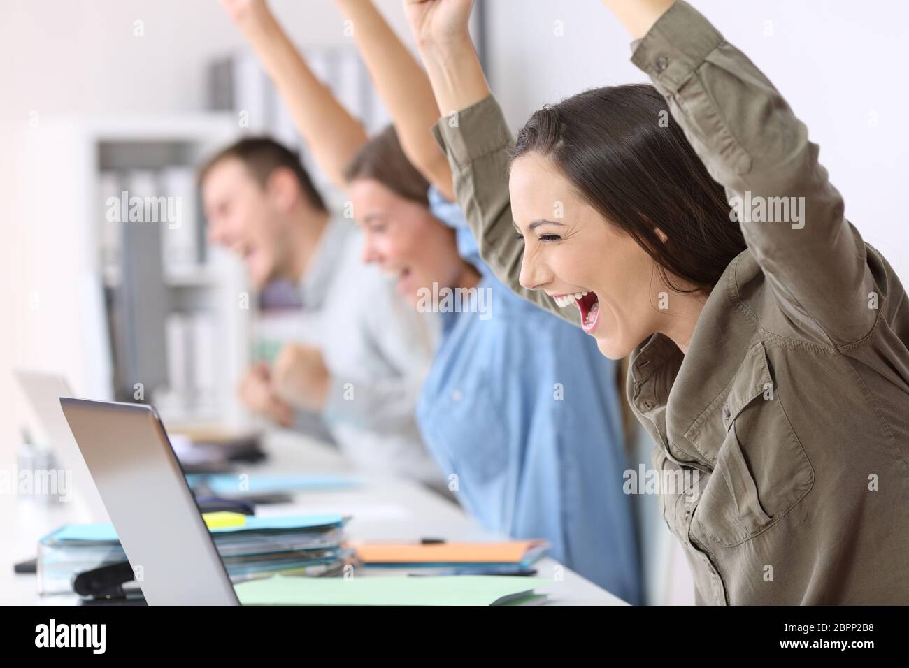 Tre dipendenti eccitati ricevendo buone notizie on line nei notebook in ufficio Foto Stock