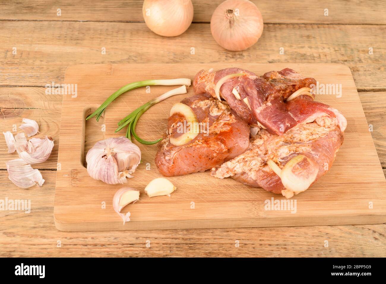 Maiale sottaceto con cipolle e aglio su un tagliere di legno. Foto Stock