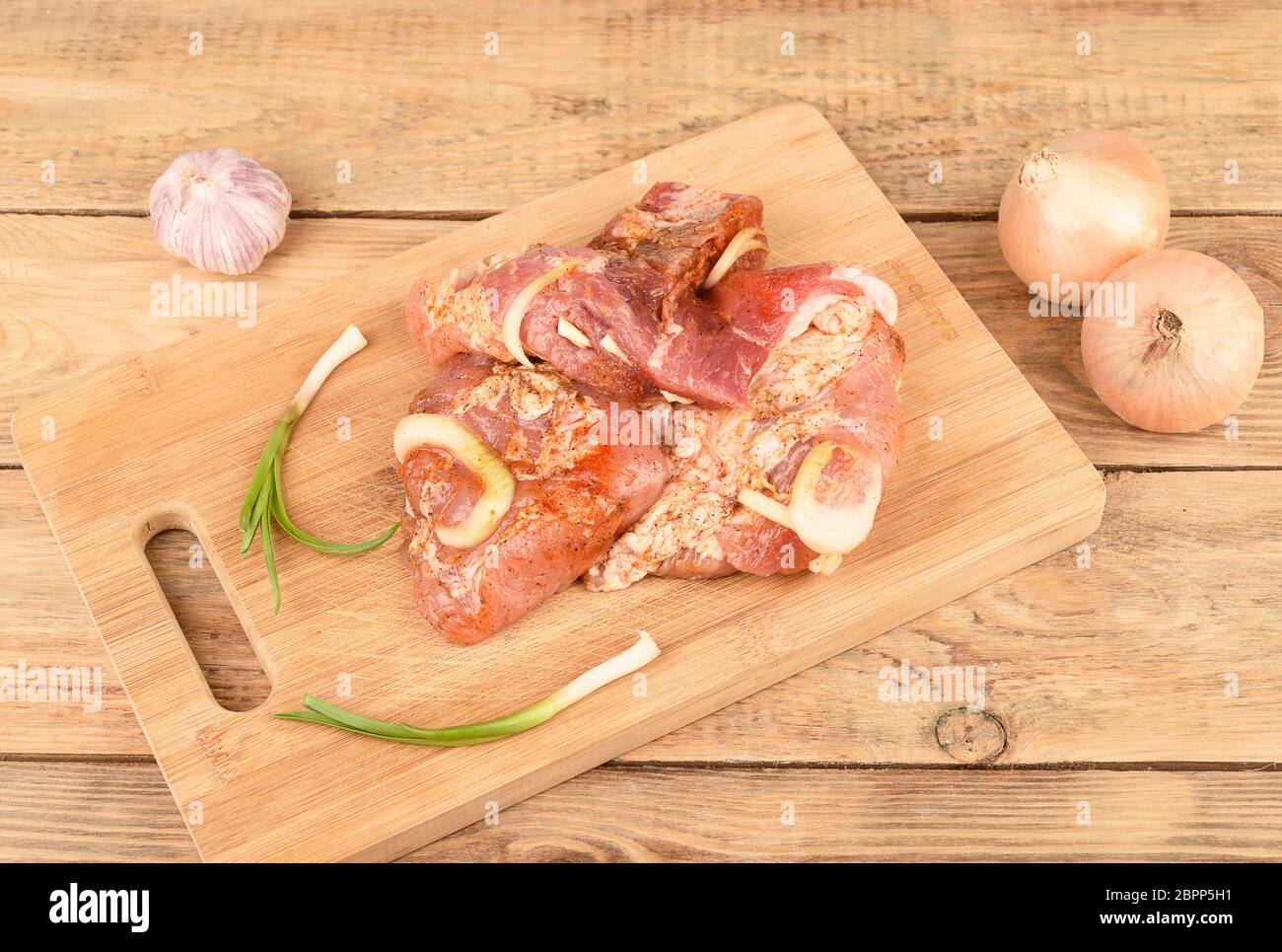 Maiale sottaceto con cipolle e aglio su un tagliere di legno. Foto Stock