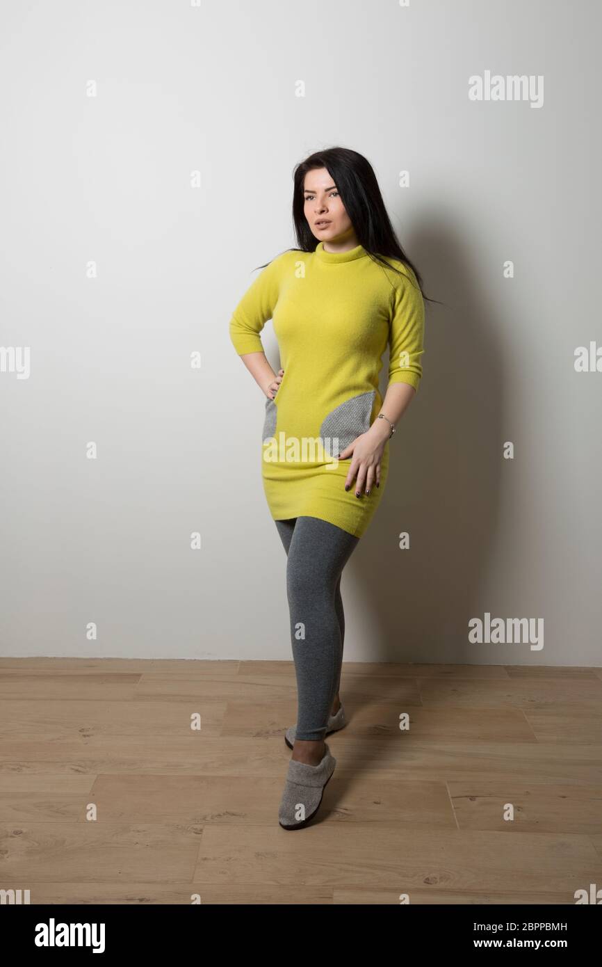 Una ragazza con un maglione lungo giallo e tasche grigie in leggings grigio  si erge su uno sfondo grigio Foto stock - Alamy