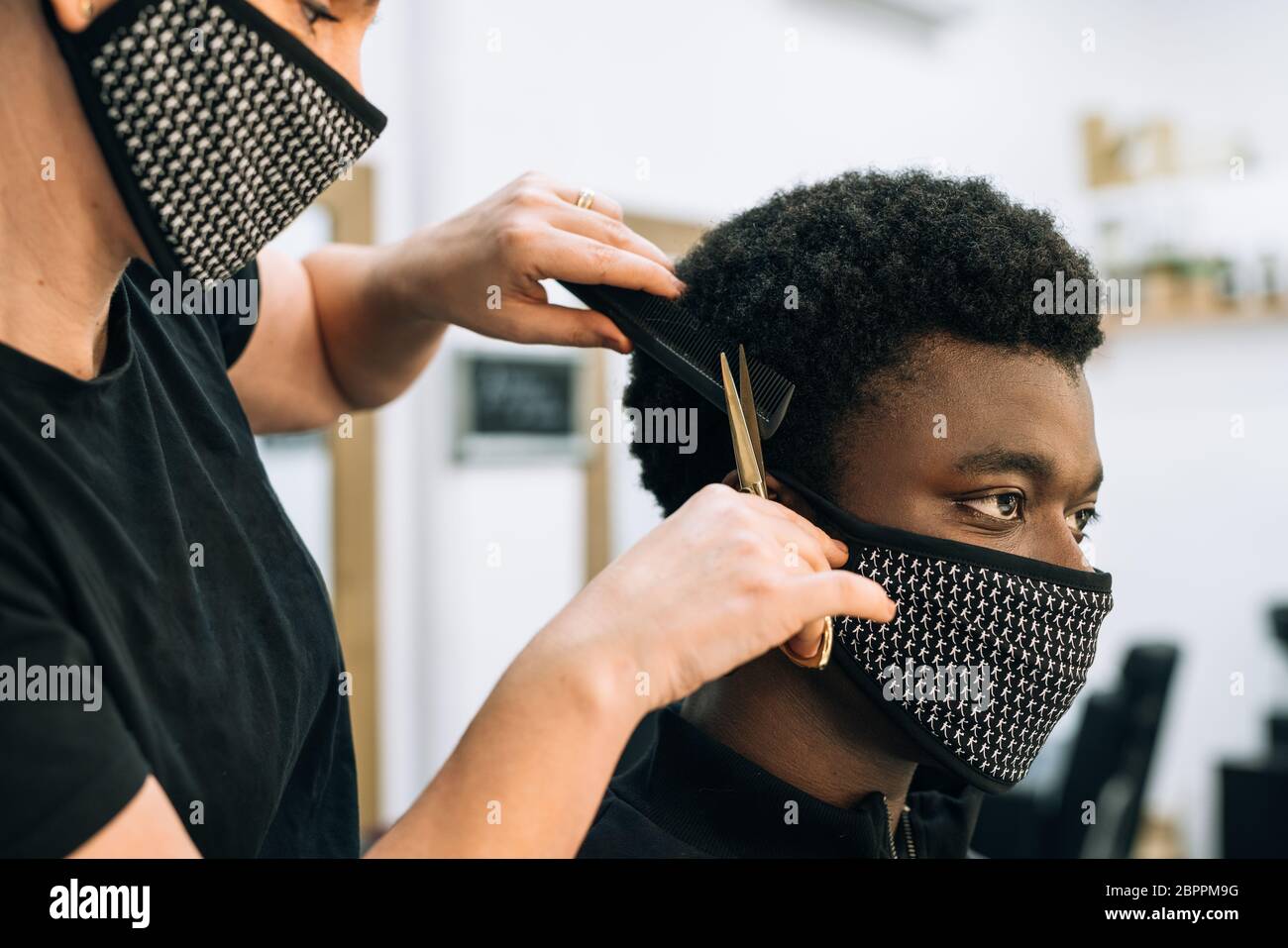 faccia di un ragazzo nero che ottiene un taglio di capelli in un salone di  capelli con una maschera nera sulla sua faccia dal coronavirus. Il  parrucchiere indossa anche una maschera. I