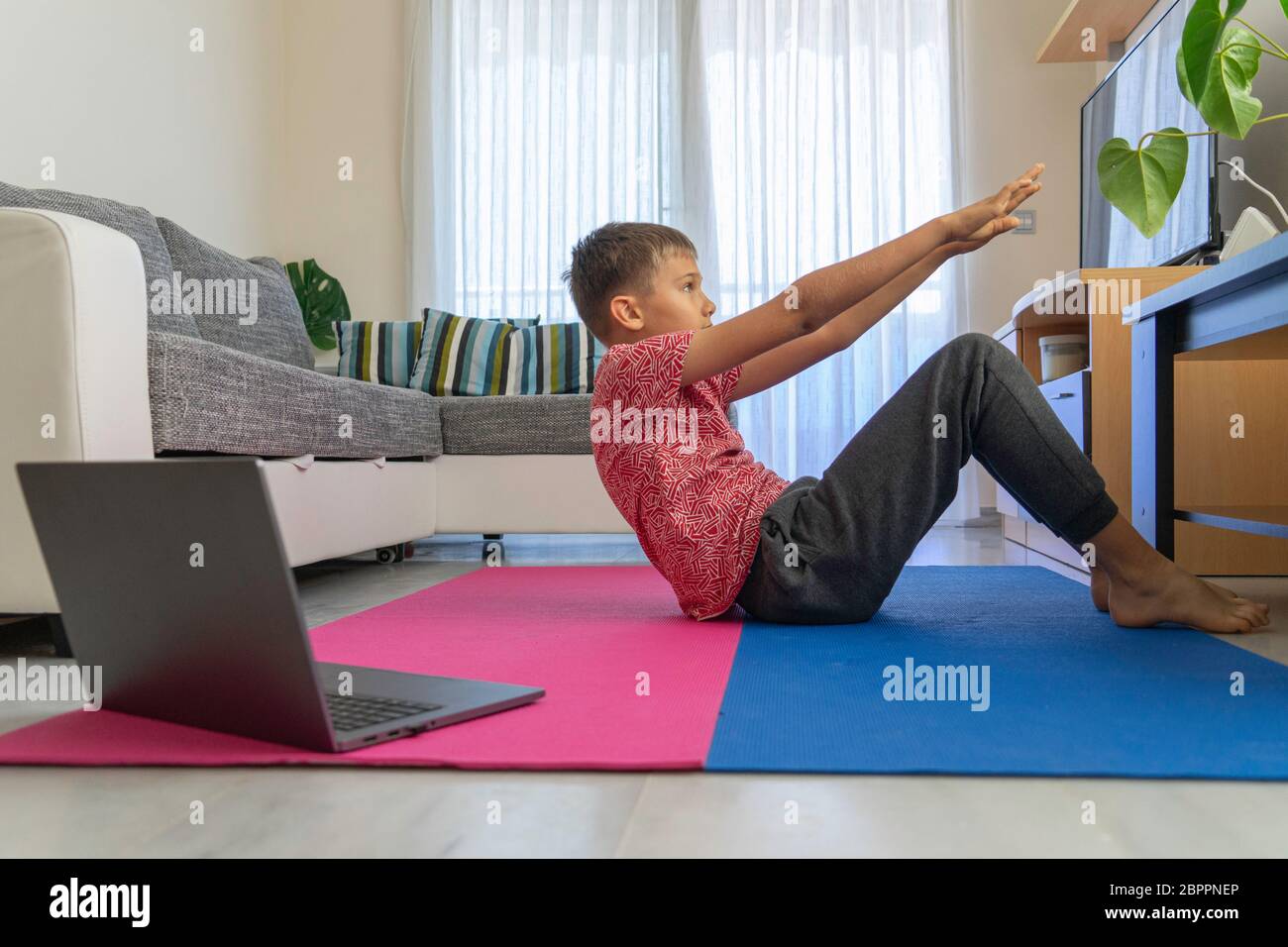 Ragazzo adolescente con computer portatile che fa esercizi sportivi, praticare yoga in soggiorno. Sport, stile di vita elegante, tempo libero attivo a casa Foto Stock