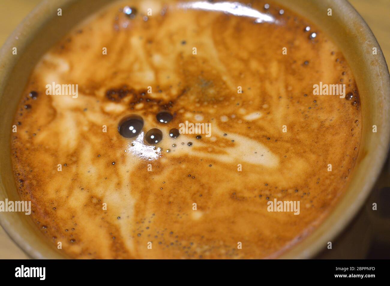 Una tazza di caffè istantaneo con un po' di latte, in primo piano con profondità di campo poco profonda. Innumerevoli piccole bolle e alcune più grandi possono essere Foto Stock
