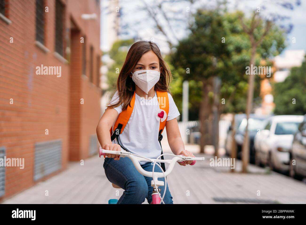Ragazza con maschere che cavalcano una bicicletta per strada durante la pandemia del coronavirus. Foto Stock