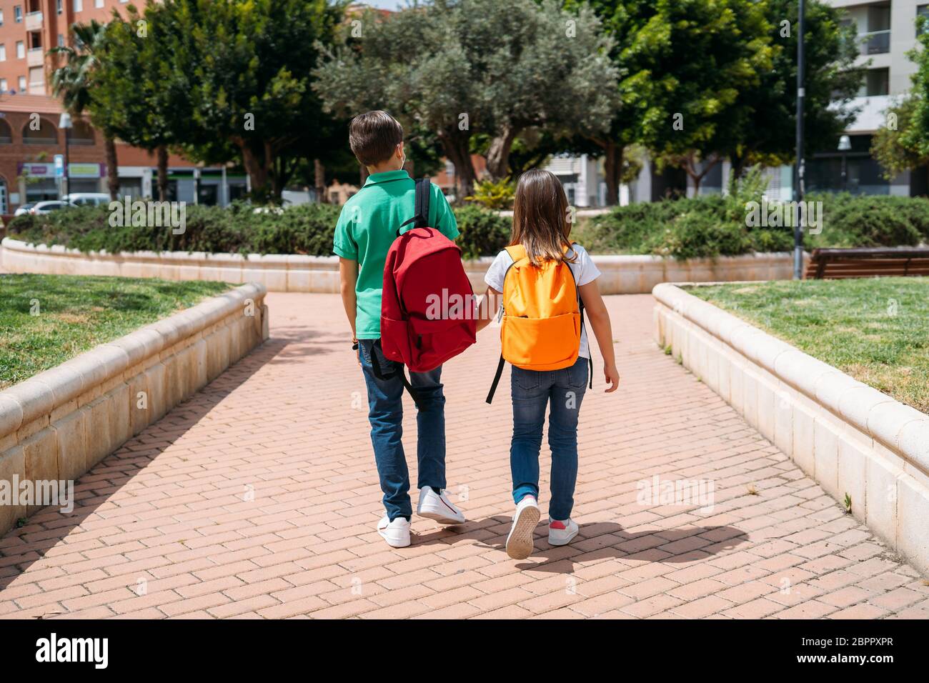 Ragazzo e ragazza con zaini e maschere che vanno a scuola in pandemia coronavirus Foto Stock