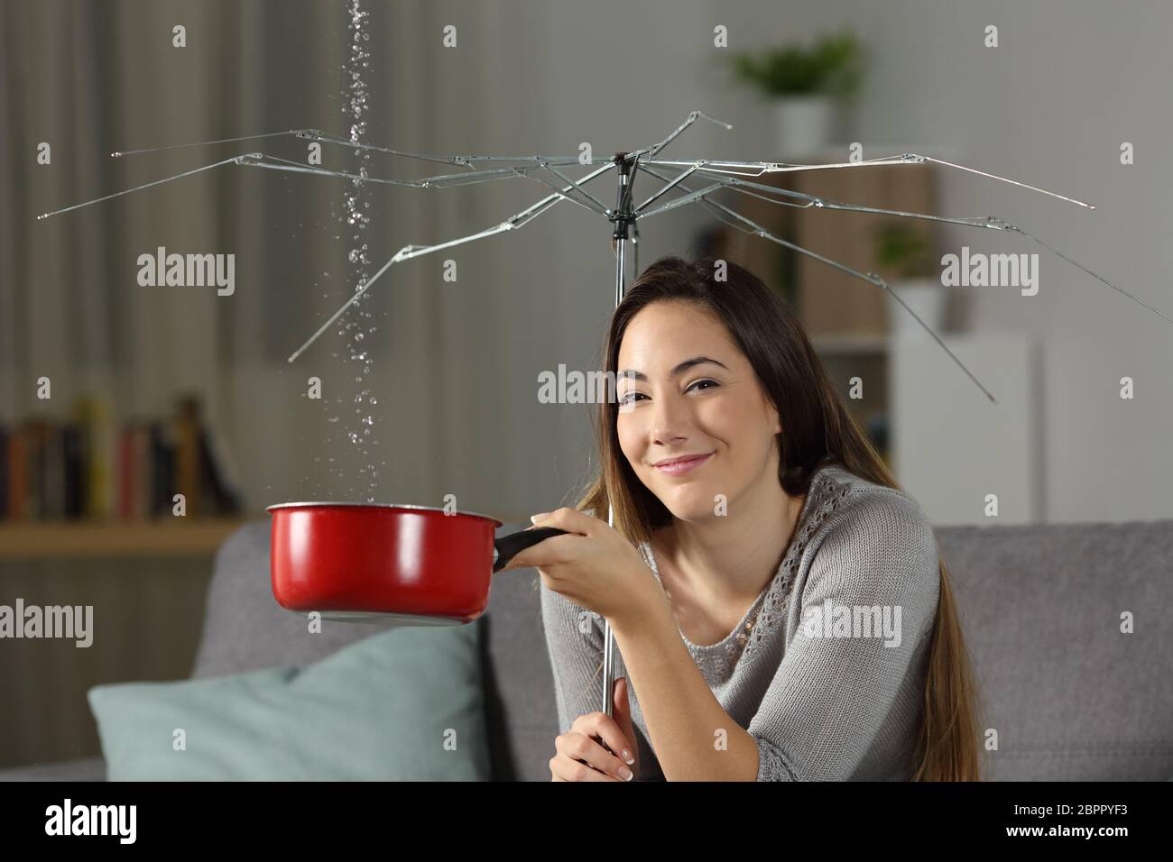 Donna positiva avente home problemi guardando la telecamera seduta su un divano nel soggiorno Foto Stock