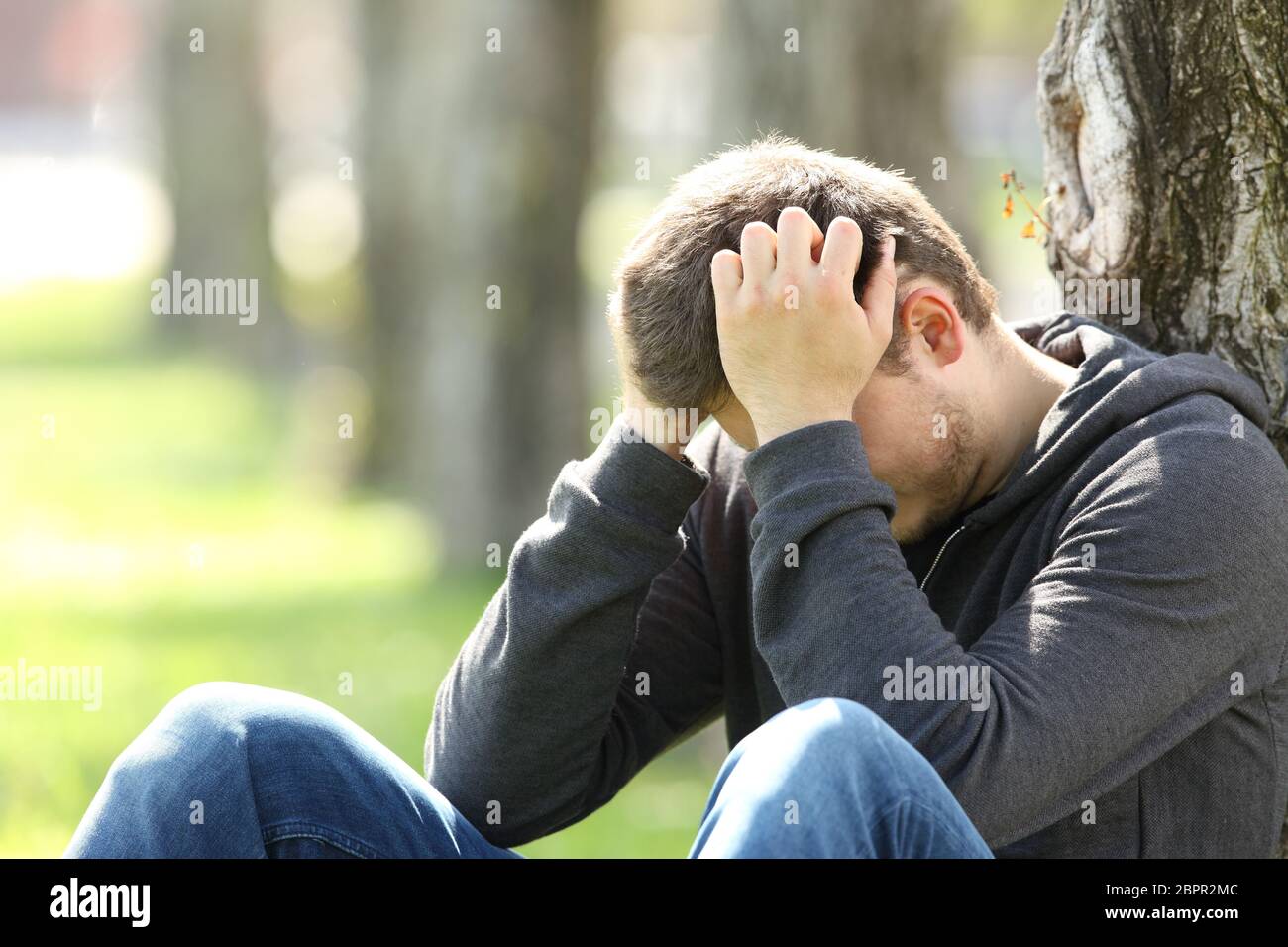 Ritratto di un unico triste teen piange seduto sul prato di un parco Foto Stock