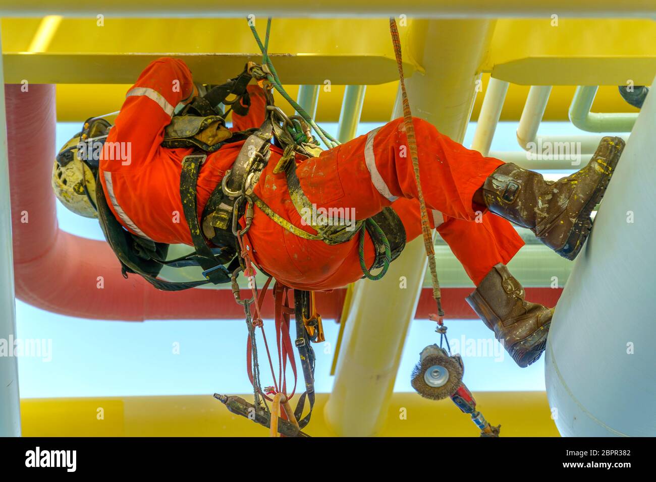 Lavoro in altezza. Una discesa dalla vista laterale con tuta sporca che indossa dispositivi di protezione individuale (PPE) appesi alle linee di vita per rimuovere le ammaccature in Foto Stock