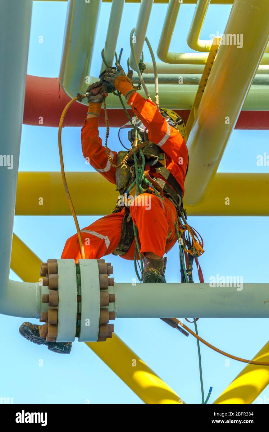 Lavoro in altezza. Una discesa dalla vista posteriore con tuta sporca che indossa dispositivi di protezione individuale (PPE) appesi alle linee di vita per rimuovere le ammaccature in Foto Stock