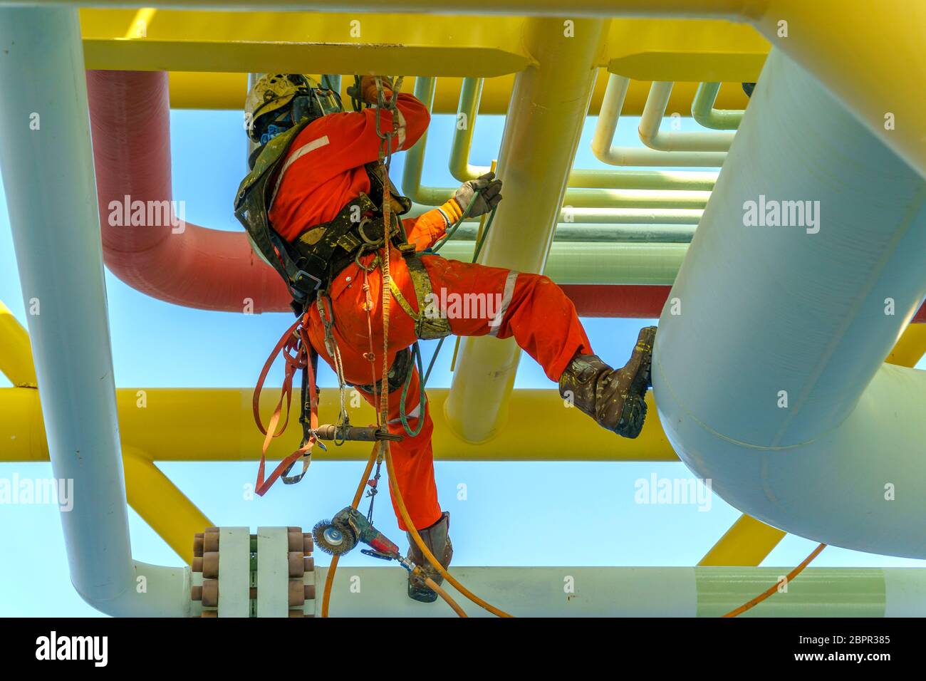 Lavoro in altezza. Una discesa dalla vista posteriore con tuta sporca che indossa dispositivi di protezione individuale (PPE) appesi alle linee di vita per rimuovere le ammaccature in Foto Stock