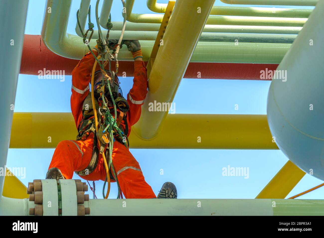 Lavoro in altezza. Una discesa dalla vista frontale con tuta sporca che indossa dispositivi di protezione individuale (PPE) appesi alle linee di vita che si stendono sulla pipeline Foto Stock