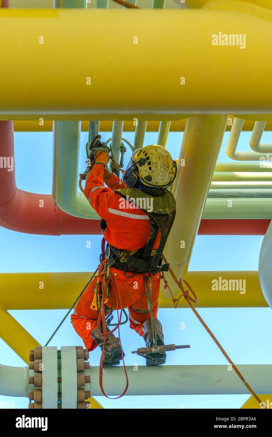 Lavoro in altezza. Una discesa dalla vista posteriore con tuta sporca che indossa dispositivi di protezione individuale (PPE) appesi alle linee di vita per rimuovere le ammaccature in Foto Stock