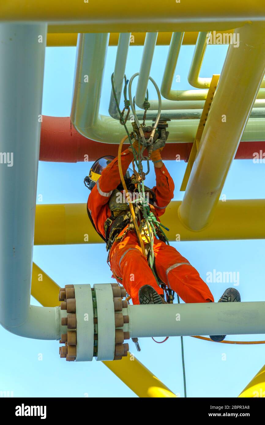 Lavoro in altezza. Una discesa dalla vista frontale con tuta sporca che indossa dispositivi di protezione individuale (DPI) appesi alle linee di vita per rimuovere le ammaccature A. Foto Stock