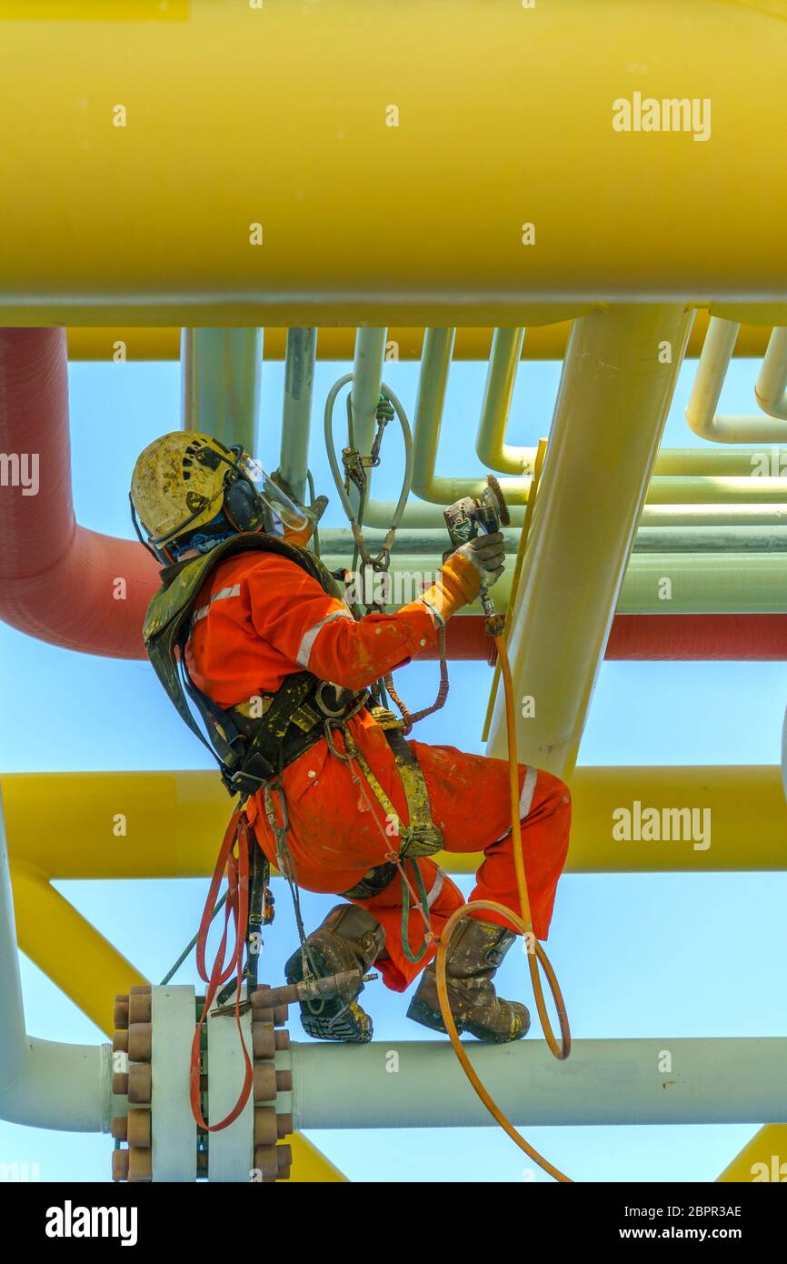 Lavoro in altezza. Una discesa dalla vista posteriore con tuta sporca che indossa dispositivi di protezione individuale (PPE) appesi alle linee di vita per rimuovere le ammaccature in Foto Stock