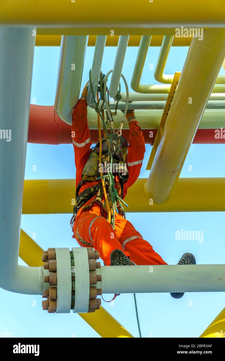 Lavoro in altezza. Una discesa dalla vista frontale con tuta sporca che indossa dispositivi di protezione individuale (DPI) appesi alle linee di vita per rimuovere le ammaccature A. Foto Stock