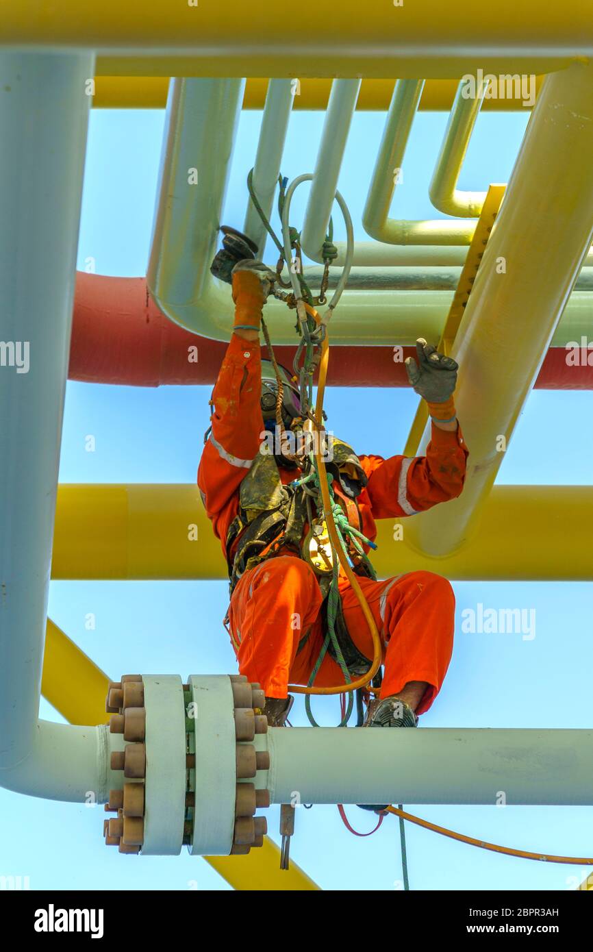 Lavoro in altezza. Una discesa dalla vista frontale con tuta sporca che indossa dispositivi di protezione individuale (DPI) appesi alle linee di vita per rimuovere le ammaccature A. Foto Stock