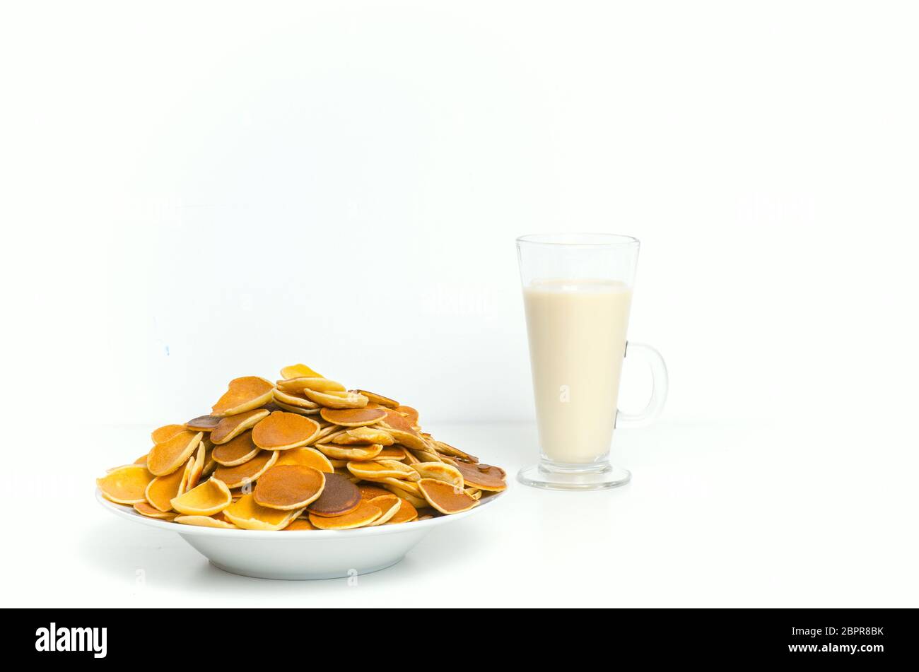 Pasto trendy con cereali pancake con latte su sfondo bianco. Minuscoli pancake al forno. Cibo per la colazione. Foto Stock