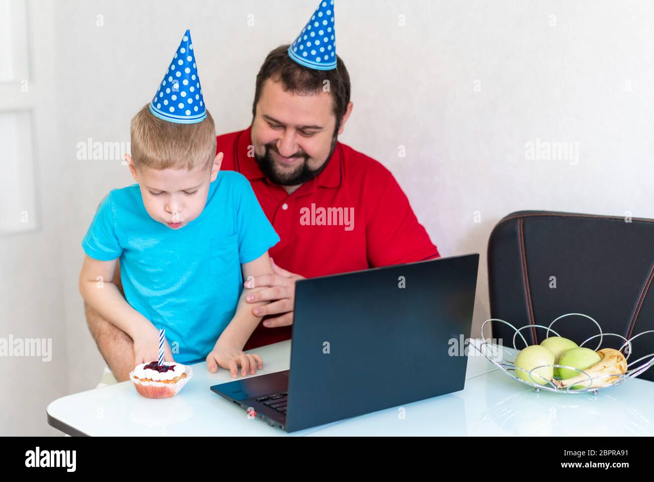 Il ragazzino con il padre festeggia il compleanno online, parlando con i parenti e gli amici. Soffia fuori la candela sulla torta Foto Stock