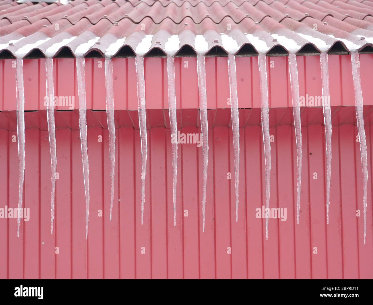Lunghi ghiaccioli sul tetto rosso Primavera Foto Stock