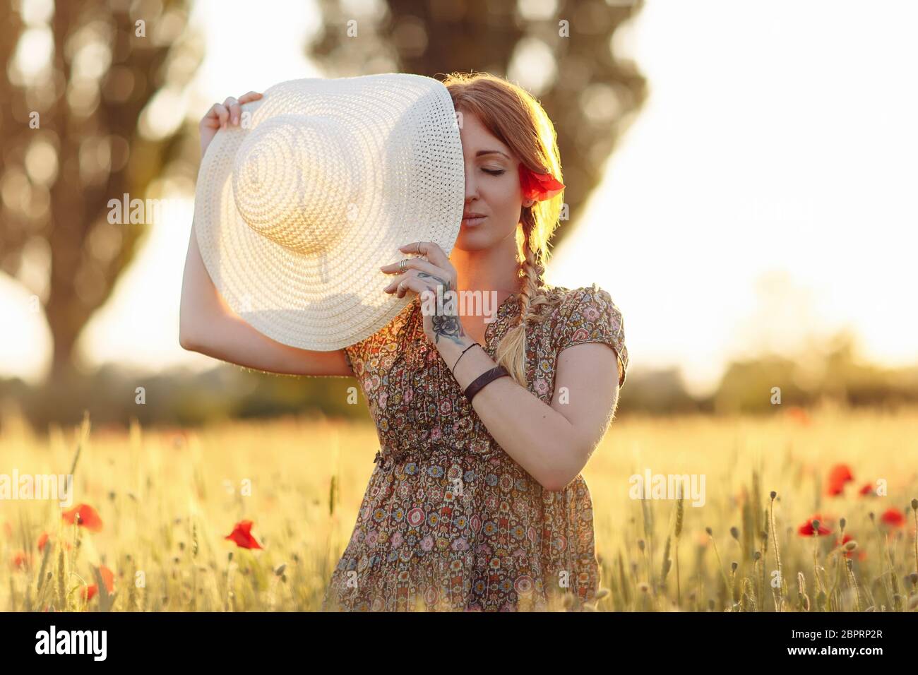 Donna rossa con cappello su campo verde con papaveri al tramonto estivo Foto Stock