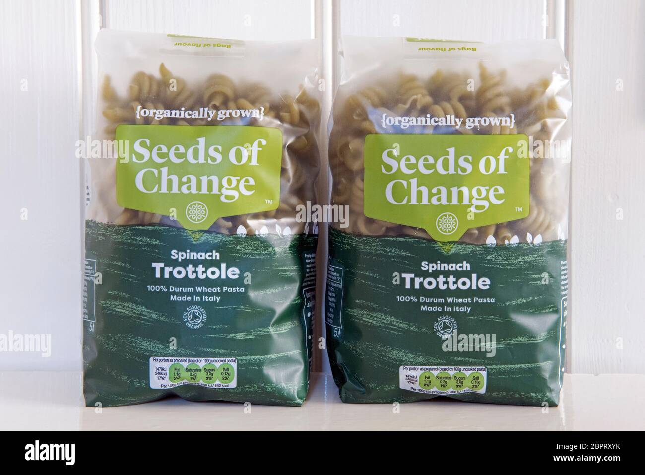 Due pacchetti di semi di Cambio spinaci di pasta coltivati organicamente Trottole pasta di grano duro su ripiano color crema contro il dorso di legno crema Foto Stock